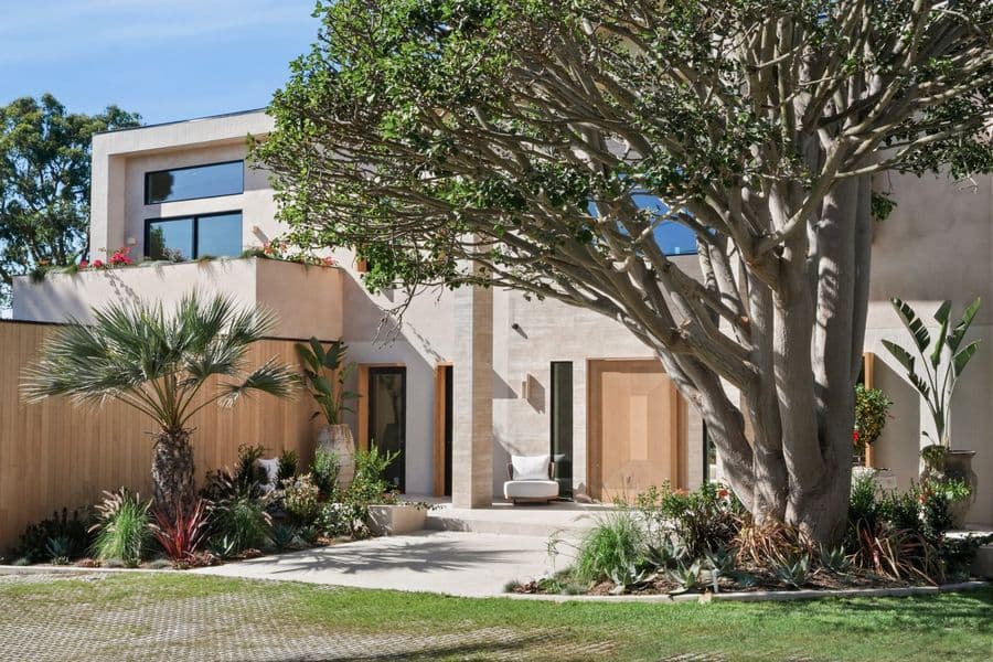 House front with an oversized oak pivot door set in vertical oak siding, under a large tree